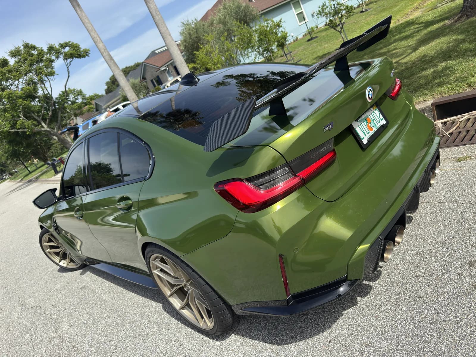 Rear of a BMW wrapped in matte green, with the factory wing kept